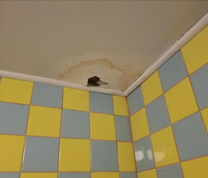 visible hole and water stain in restroom ceiling